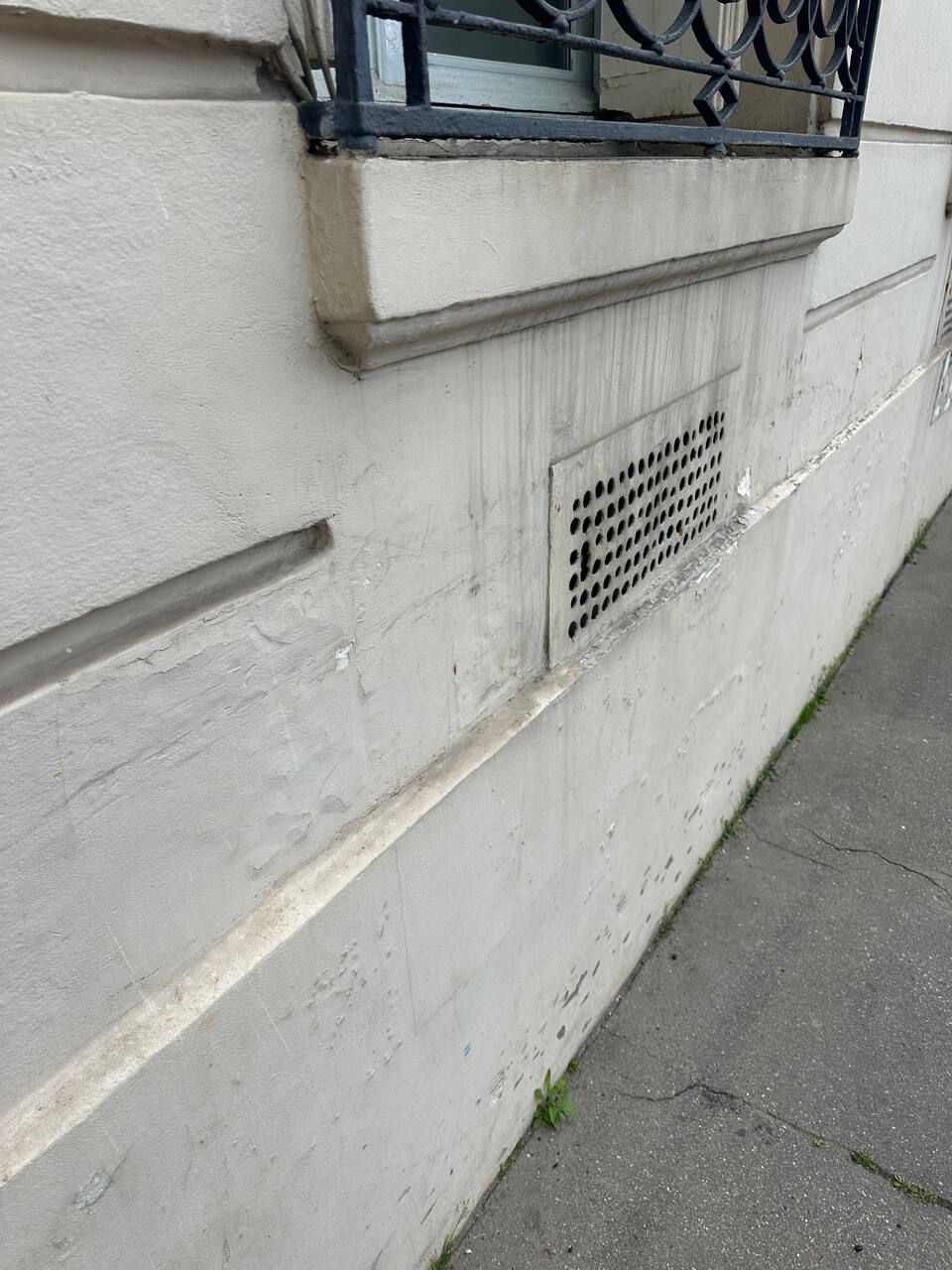 Bas de façade ancienne avec traces verticales sous appui de fenêtre et grille de ventilation encrassée